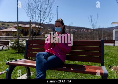 Une belle femme est assise dans un parc sur un banc et utilisation d'un téléphone cellulaire Banque D'Images