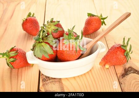 Beaucoup de fraises sucrées dans un bol en céramique clair avec une cuillère en bois, sur une table en bois. Banque D'Images