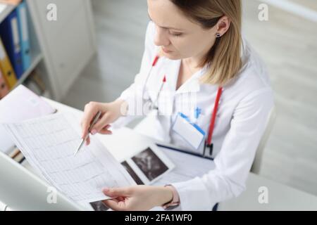 Médecin assis à table et regardant le cardiogramme en clinique Banque D'Images