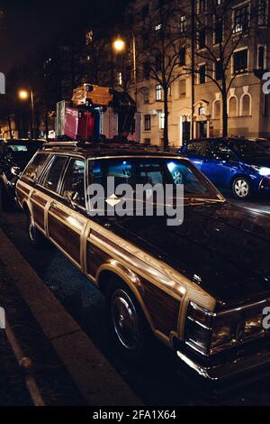 La vieille voiture marron est parking avec des bagages colorés sur le dessus pendant Noël à Munich, Bavière, Allemagne. Les lampadaires reflètent la lumière dans la lacque. Banque D'Images