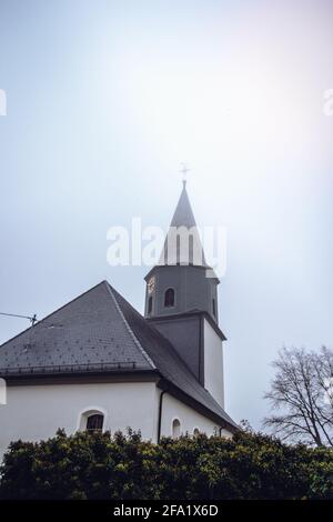 Église blanche et grise avec un gloriole à Feldstetten, en allemagne. Des buissons remplissent le premier plan de la chapelle. Au sommet du kirktower se trouve une croix dorée Banque D'Images