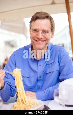 Beau caucasien mangeant des spaghetti au restaurant extérieur italien Banque D'Images