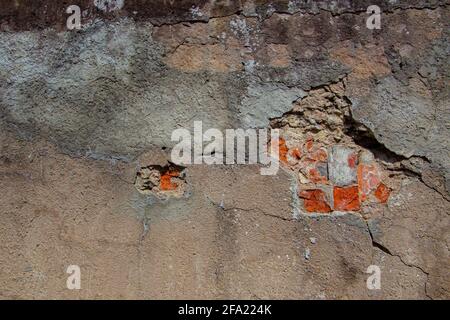 Mur en béton gris endommagé avec trou dans le plâtre visible la brique rouge underneith Banque D'Images