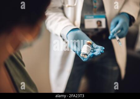 Gros plan d'un médecin présentant un flacon de vaccin Covid-19 à la maison. Professionnel de la santé donnant la vaccination à la femme pendant une pandémie. Banque D'Images