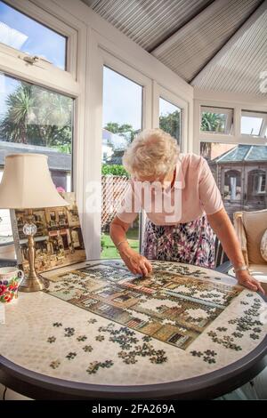 Femme âgée dans ses années 70 faisant un puzzle à sa résidence, Angleterre, Royaume-Uni Banque D'Images