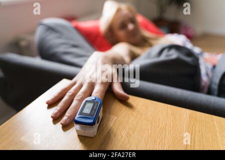 Femme d'âge moyen à la maison vérifiant le niveau d'oxygène dans le sang à l'aide d'un oxymètre de pouls. Coronavirus symptômes covid. Asthme, déconfort des poumons. Banque D'Images