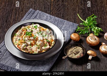 stroganoff de foie de champignon et de veau dans un bol noir une table rustique en bois sombre avec des ingrédients et des épices Banque D'Images