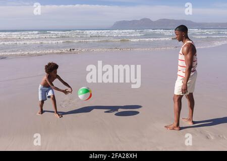 Père et fils afro-américains s'amusant à jouer avec le ballon à la plage Banque D'Images