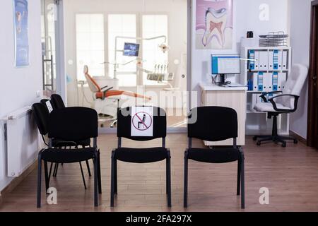 Aire d'attente vide, réception de stomatologie avec personne dans elle avec nouvelle normale ayant signe sur la chaise pour la distance sociale pendant l'épidémie de Covid-19. Salle d'attente dentaire moderne équipée en période d'épidémie Banque D'Images