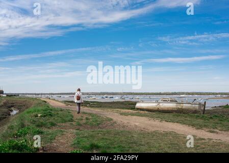 Essex Coast UK, vue arrière d'une femme marchant seule sur le chemin côtier le long de la rivière Blackwater, Mersea Island, Essex, Royaume-Uni Banque D'Images
