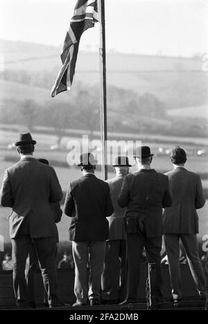 Royaume-Uni, Angleterre, Devonshire, Buckfastleigh, 1972. Des courses point à point ont eu lieu à Dean court sur les Dean Marshes, près de l'A38 entre Plymouth et Exeter. Trois stewards portant des chapeaux melons noirs dans le centre et d'autres spectateurs regardant une course sous le drapeau de l'Union ou drapeau de l'Union du Royaume-Uni. Banque D'Images