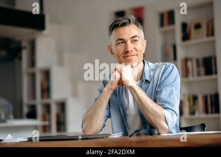 Portrait d'une personne heureuse et élégante, originaire de race blanche, pigiste ou Manager, vêtue avec élégance, assise à la table, prenant une pause au travail, rêvant de vacances, regardant loin, se joignant aux mains Banque D'Images
