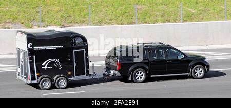 Vue panoramique latérale d'une voiture noire tractant un cheval hongrois noir Liberte calèche route animale remorque de transport le long de l'anglais Autoroute britannique Banque D'Images