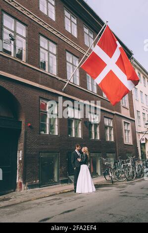 Copenhague, Danemark 11 juin 2019. Couple de mariage marchant dans la rue sur le fond du drapeau du Danemark. Banque D'Images