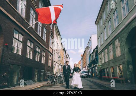 Copenhague, Danemark 11 juin 2019. Couple de mariage marchant dans la rue sur le fond du drapeau du Danemark. Banque D'Images