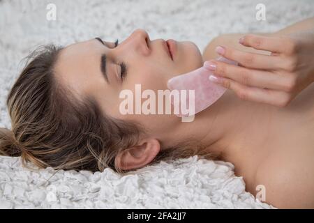 Jeune et belle femme pendant le massage traditionnel chinois - Gua Sha avec pierre. Gros plan. Soins de beauté dans le salon DE SPA. Soins de la peau anti-âge Banque D'Images