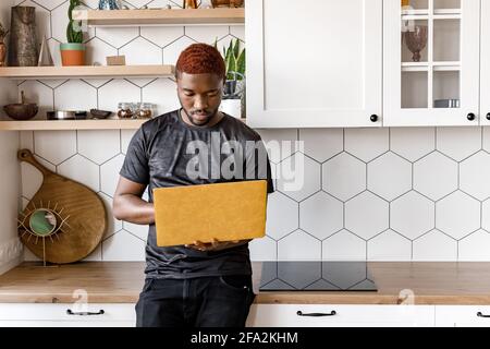 Un travailleur indépendant sérieux est debout dans la cuisine à la maison, en utilisant un ordinateur portable, travaillant sur un projet sérieux. Un jeune homme d'affaires concentré qui réfléchit aux idées Banque D'Images