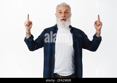 Surpris homme mûr à l'étonnement, pointant les doigts vers le haut et montrant promo affaire, afficher la publicité, se tenant sur fond blanc Banque D'Images