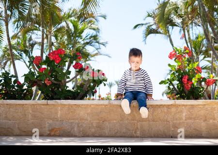 Petit garçon enfant assis sur un banc dans le parc Banque D'Images