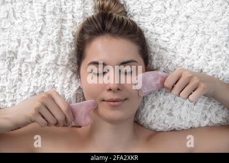 Jeune et belle femme pendant le massage traditionnel chinois - Gua Sha avec pierre. Gros plan. Soins de beauté à la maison. Anti-âge soin de la peau avec Banque D'Images