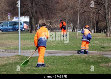 Les concierges nettoient les rues et les pelouses de la ville de printemps. Balayeuses avec râteau et balai, travaux de logement et services communautaires Banque D'Images