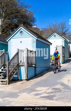 Cycliste haut en couleur, passant devant des cabanes de plage à Alum Chine, Bournemouth, Dorset, Royaume-Uni, le jour ensoleillé d'avril Banque D'Images