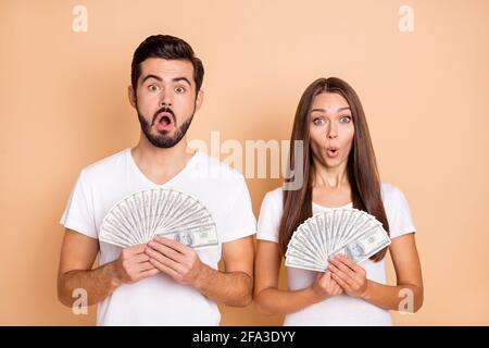 Photo de drôle impressionné couple marié habillé blanc t-shirts gagner casino grande quantité argent isolé beige couleur fond Banque D'Images