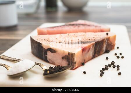 Espadon brut. Deux morceaux de biftecks de poisson frais crus avec sel et poivre noir se trouvent sur une planche à découper en marbre sur fond en bois Banque D'Images