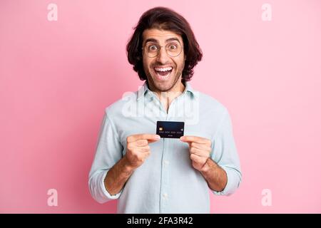 Portrait de jeune beau excité souriant fou homme gars mâle tenir la carte de crédit porter des lunettes isolées sur fond de couleur rose Banque D'Images