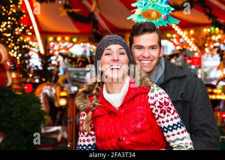 Homme et femme ou un couple ou des amis pendant l'avènement saison ou vacances en face d'un carrousel ou d'un manège Sur le marché de Noël ou de Noël Banque D'Images