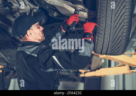 Caucasien Automotive Mechanic dans ses années 30 Remplacement des éléments de suspension de voiture à l'intérieur de la station-service autorisée de la concession. Thème de l'industrie du transport Banque D'Images