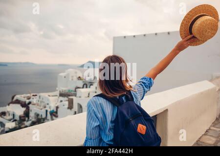 Femme touristique marchant sur l'île de Santorini, Grèce appréciant la mer et le paysage d'architecture de ville. Voyageur avec sac à dos admire Caldera vue à Oia Banque D'Images