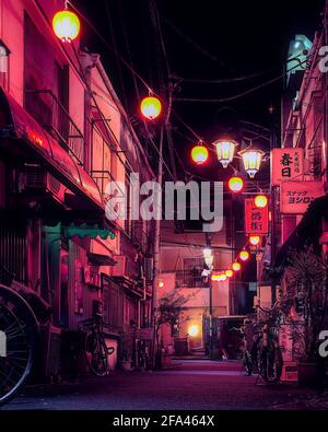 Tokyo, Japon - novembre 9 2020 : vue nocturne d'une petite allée de Tokyo illuminée par des lanternes en papier rosé, avec plusieurs bicyclettes visibles Banque D'Images