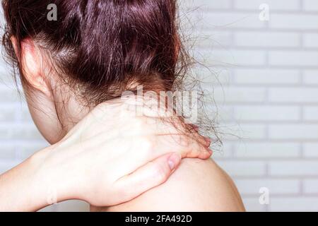 Jeune femme caucasienne avec la main sur son cou et son épaule malsains. Concept d'auto-massage, de syndrome de bureau, de mal de cou et de douleur musclar. Banque D'Images