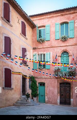 Roussillon, Vaucluse, France; 24 juillet 2018: Bâtiment de couleur ocre avec volets en bois colorés sur la place principale de la ville Banque D'Images