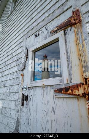 Un mur extérieur en bois usé blanc avec un panneau étroit. Au centre du mur, il y a une fenêtre en verre avec un reflet d'un phare. Banque D'Images