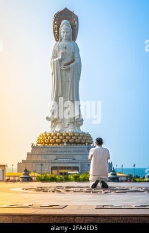 Moine méconnaissable priant devant le Guanyin de 108m de haut Statue de la mer du Sud du temple du parc culturel du bouddhisme de Nanshan Au lever du soleil à Sanya à Hain Banque D'Images