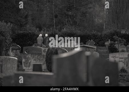 Umkirch, Allemagne - 24 décembre 2014 : couple de personnes âgées rendant hommage devant une tombe dans un cimetière derrière une église catholique. Banque D'Images