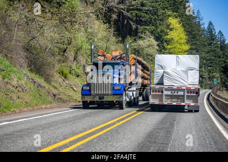 Différents semi-camions chargés classiques avec semi-remorques déplacement dans des directions opposées sur la route sinueuse étroite avec forêt verte sur la sid Banque D'Images