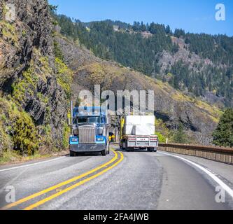 Différents semi-camions chargés classiques avec semi-remorques déplacement dans des directions opposées sur la route sinueuse étroite avec tunnel et rocher sur le Banque D'Images