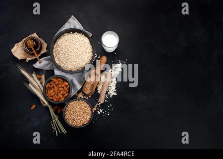 Flocons d'avoine roulés dans des bols noirs et épis de blé doré sur fond sombre. Vue de dessus, espace de copie Banque D'Images