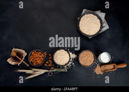 Flocons d'avoine roulés dans des bols noirs et épis de blé doré sur fond sombre. Vue de dessus, espace de copie Banque D'Images