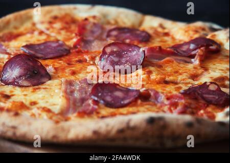Délicieuse pizza maison sur une assiette en bois contre le noir arrière-plan Banque D'Images