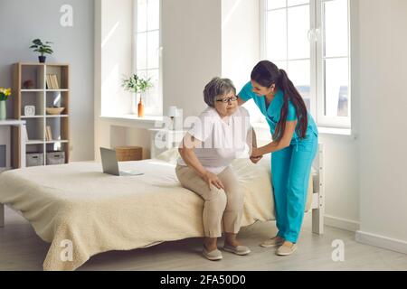 Une femme soignante qui s'occupe d'une femme âgée dans une maison de soins infirmiers l'aide à sortir du lit. Banque D'Images