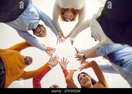 Prise de vue en contre-angle de personnes variées et heureuses, debout dans un cercle, se joignant aux mains et souriant Banque D'Images