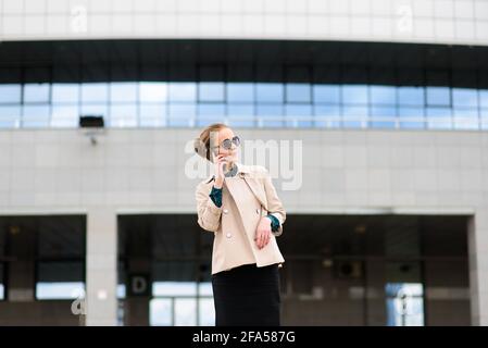 Jeune femme d'affaires belle avec des lunettes de soleil, téléphone, ordinateur portable, tasse de café dans la rue de la ville Banque D'Images