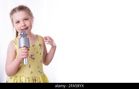 Une petite fille blonde chante une chanson dans un microphone dans ses mains. Un bel enfant montre ses émotions sincères de bonheur et de positif. Cheveux tressés Banque D'Images