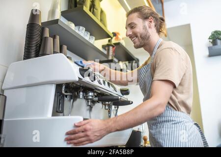 Homme joyeux dans un tablier essuyant machine à café Banque D'Images