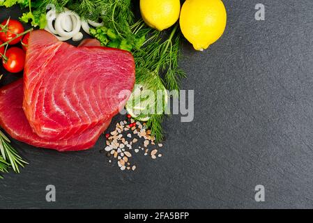 Thon cru Steak, thon sashimi, thon poisson tranché avec des légumes. Manger sainement avec des fruits de mer, nous cuisons à la maison. Disposition de la viande de poisson sur pierre noire Banque D'Images