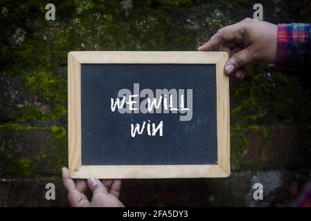 Main avec ardoise écrit "NOUS ALLONS GAGNER" sur le courant du coronavirus scénario Banque D'Images